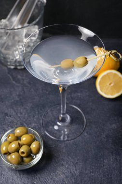 Bir bardak lezzetli martini, koyu arkaplanda limon ve yeşil zeytin, yakın plan.