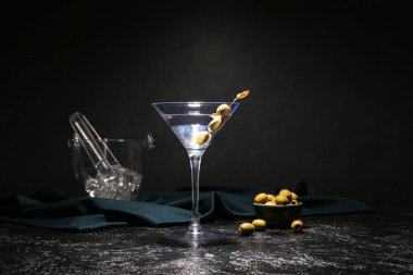 Koyu arkaplanda yeşil zeytinli ve buzlu bir bardak lezzetli martini.