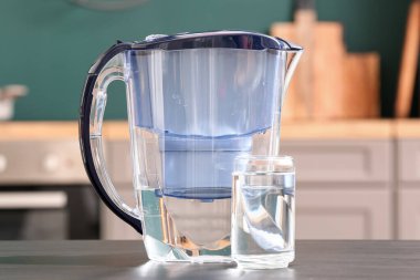 Modern filtre sürahi ve bir bardak su mutfaktaki siyah masada.