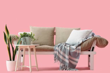 Pembe arka planda yastıklı ve ekoseli rahat gri kanepe.