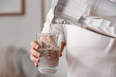 Kadın filtre sürahisinden bardağa saf su döküyor.