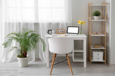 Modern dizüstü bilgisayarı ve pencerenin yanında güzel narsist çiçekleri olan rahat bir iş yeri.