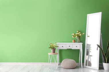 Yeşil duvarın yanında lale çiçekli ve şık aynalı bir masa.