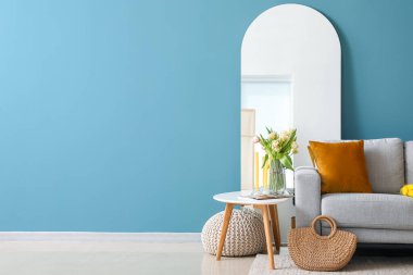 Mavi duvarın yanında rahat gri kanepesi ve aynası olan şık bir oturma odası.