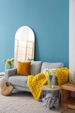 Mavi duvarın yanında rahat gri kanepesi ve aynası olan şık bir oturma odası.