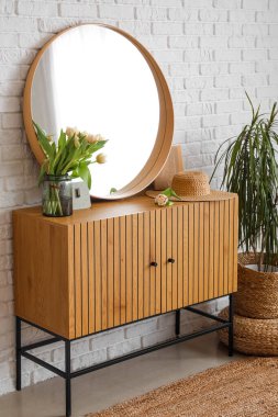 Beyaz tuğla duvarın yanında ayna ve lale çiçekleriyle süslü bir dolap.