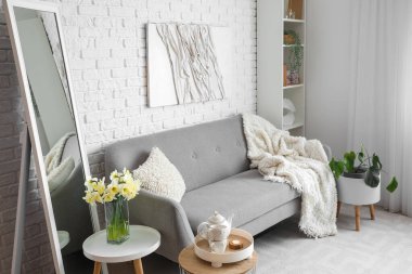 Beyaz tuğla duvarın yanında büyük aynalı ve rahat kanepeli şık bir oturma odası.