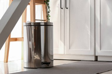 Modern mutfakta yerde metal çöp kutusu var.