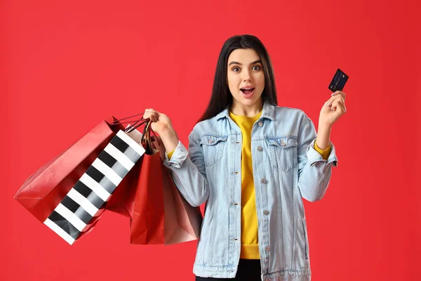 Verrast Jonge Vrouw Met Boodschappentassen Creditcard Rode Achtergrond — Stockfoto