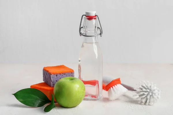 stock image Bottle of vinegar, brushes, sponges and apple on light background