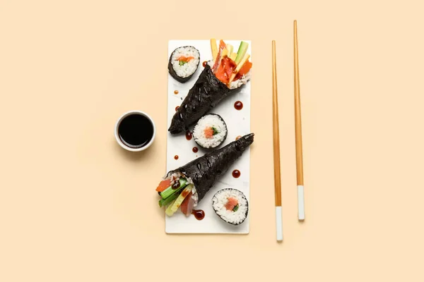 stock image Board with tasty sushi cones, rolls, soy sauce and chopsticks on color background