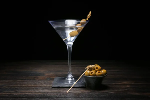 stock image Glass of tasty martini and green olives on dark wooden table