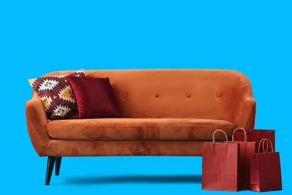 Przytulna Brązowa Sofa Poduszkami Torbami Zakupy Niebieskim Tle — Zdjęcie stockowe
