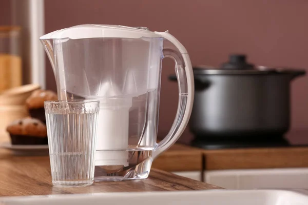 Glass of pure water and filter jug on wooden kitchen counter