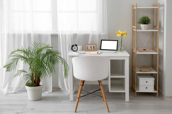 Comfortable workplace with modern laptop and beautiful narcissus flowers near window