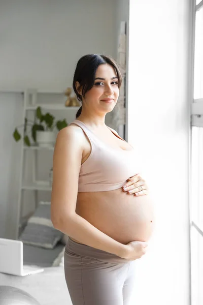 stock image Sporty young pregnant woman near window at home