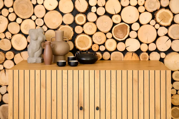 木製の壁の近くの引き出しの胸にカップや装飾が施されたティーポット — ストック写真