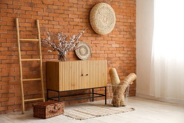 Kahverengi tuğla duvarın yanındaki vazoda çiçek açan ağaç dalları olan şık ahşap dolap.