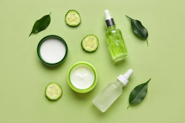 Yeşil zemin üzerinde doğal kozmetik ürünleri, bitki yaprakları ve salatalık dilimleri olan kompozisyon