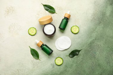 Doğal kozmetik ürünleri, pamuk pedleri, salatalık dilimleri ve grunge arkaplanda bitki yaprakları olan kompozisyon