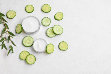 Doğal krema kavanozları, salatalık dilimleri ve açık arkaplanda okaliptüs dalıyla kompozisyon