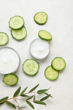 Doğal krema kavanozları, salatalık dilimleri ve açık arkaplanda okaliptüs dalıyla kompozisyon