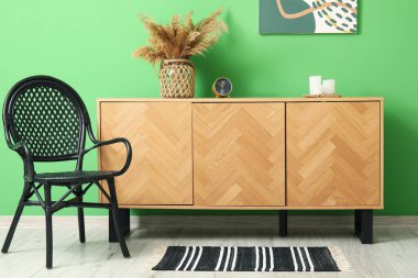 Şık ahşap dolap ve yeşil duvarın yanındaki siyah koltuk.