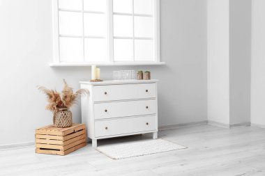 Pencere kenarındaki kutuda pampa otu olan beyaz çekmeceler ve vazolar.