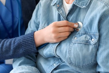 Genç bakıcı, evde steteskobu olan yaşlı bir bayanı yakından duyuyor.