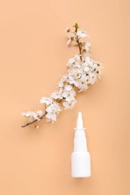 Bej arka planda çiçek açan bir dalla burun damlası. Mevsimsel alerji kavramı