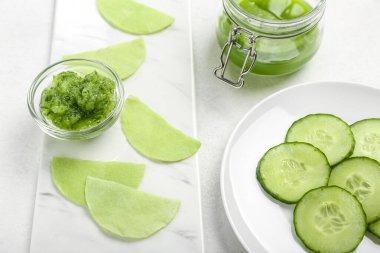 Beyaz masa üzerinde salatalık dilimleri olan pamuklu göz altı bantları, yakın plan.