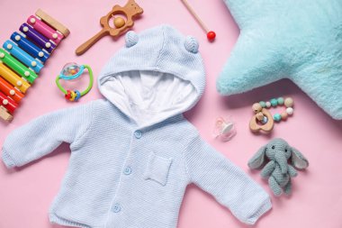 Bebek kıyafetleri ve açık pembe arka planda oyuncaklarla kompozisyon