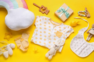 Bebek kıyafetleri ve sarı arka planda oyuncakları olan kompozisyon