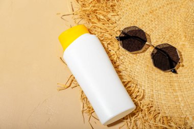 Bej arka planda güneş kremi, yaz şapkası ve güneş gözlüğü ile yaratıcı kompozisyon