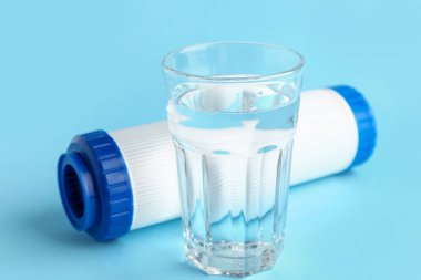 Mavi arkaplanda bir bardak sıvı ve su filtresi var.