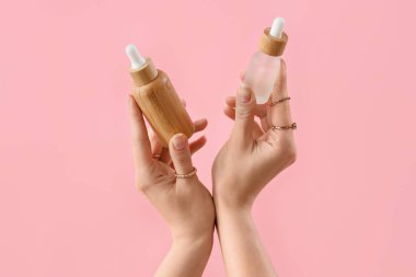 Pembe arka planda kozmetik ürünleri tutan eller