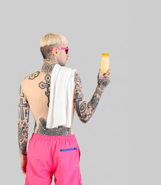Tattooed man with sunscreen cream on light background, back view