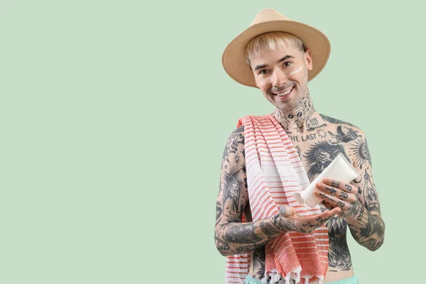 Tattooed man applying sunscreen cream on light green background
