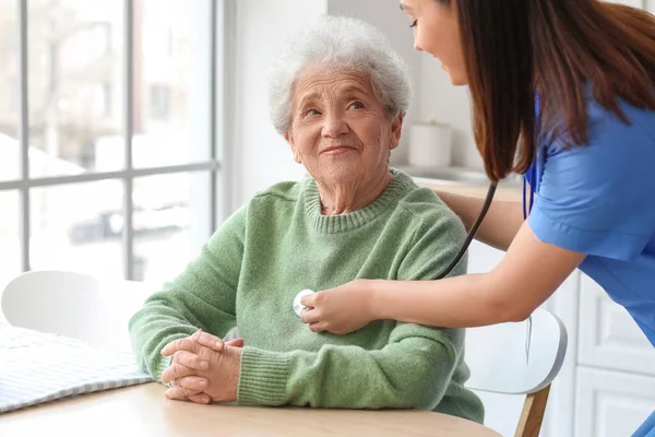 Young Caregiver Hearing Senior Woman Stethoscope Kitchen — Stock Photo, Image