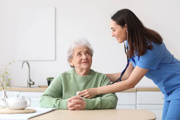 Young Caregiver Hearing Senior Woman Stethoscope Kitchen — Stock Photo, Image