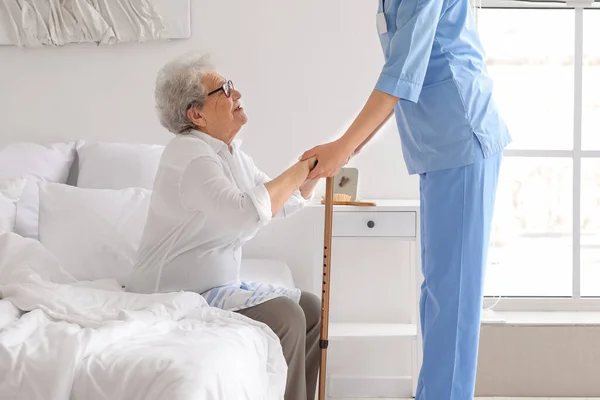 나이든 여자가 막대기를 침실에서 일어나도록 돌보는 간호사 — 스톡 사진