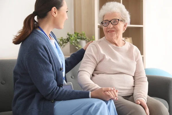 Young caregiver with senior woman holding hands at home