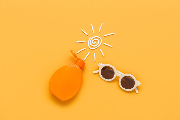 Drawings of sun made with sunscreen cream and sunglasses on orange background