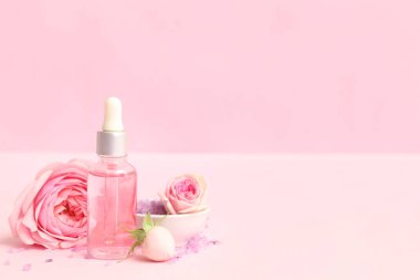 Gül özü ve pembe arka planda çiçekler olan bir şişe kozmetik yağı.