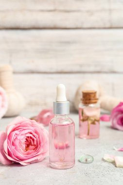 Gül özü ve beyaz masa üzerinde çiçekler olan kozmetik yağı şişeleri.