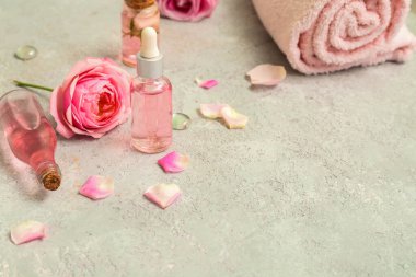 Gül özü ve beyaz masa üzerinde çiçekler olan kozmetik yağı şişeleri.