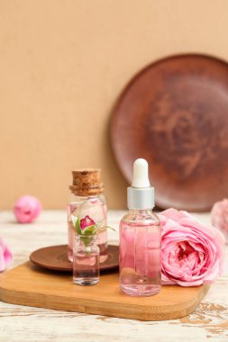 Gül özlü kozmetik yağı şişeleri ve açık ahşap masa üzerinde çiçekler.