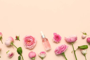 Gül özlü bir şişe kozmetik yağı ve bej arka planda çiçekler.