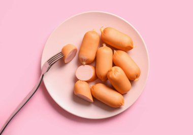 Pembe arka planda kaynamış sosis tabağı.