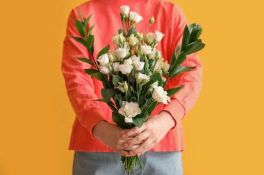 Sarı arka planda bir buket güzel Eustoma çiçeğiyle genç bir kadın.